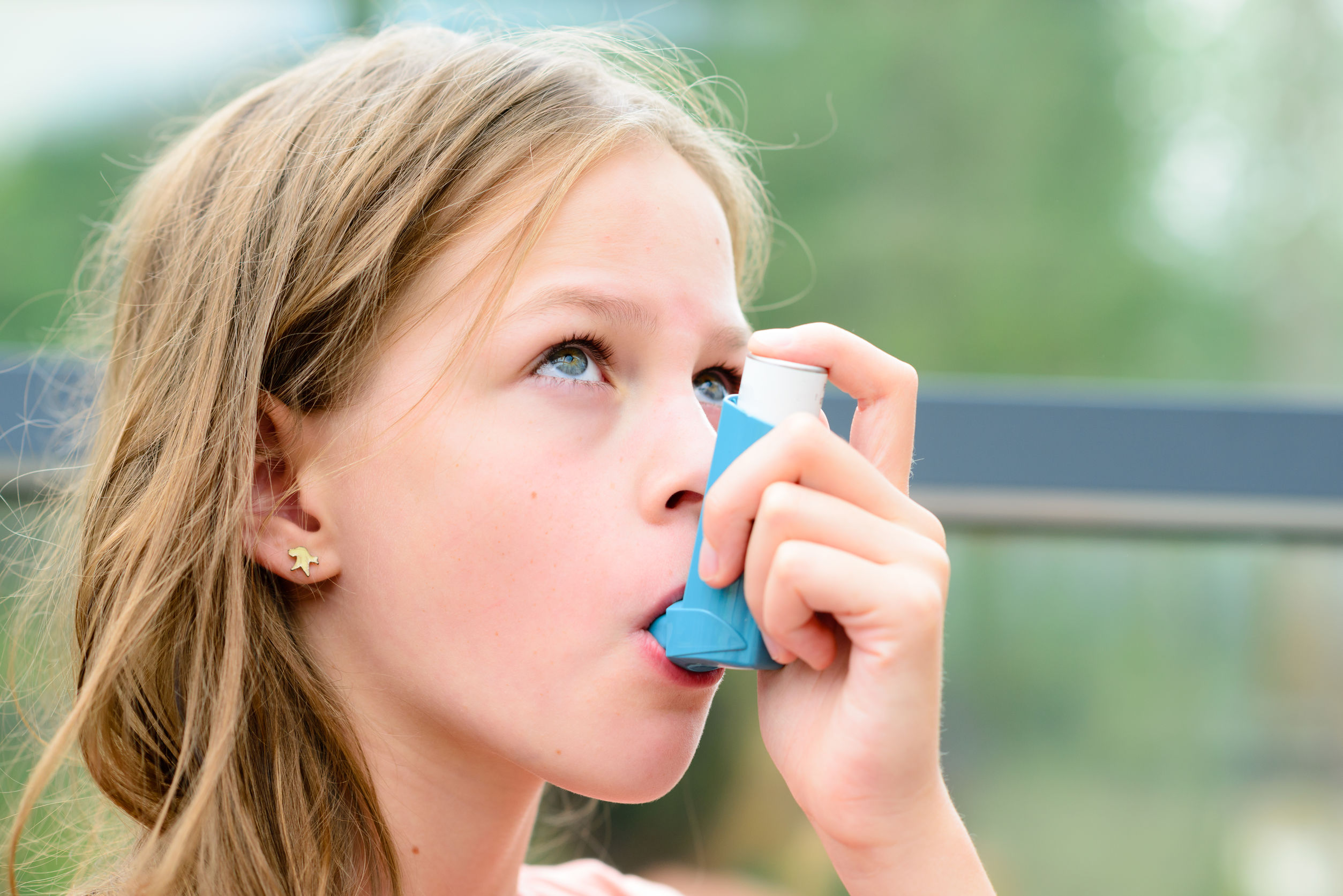 Girl having asthma using the asthma inhaler for being healthy - shallow depth of field - asthma allergy concept