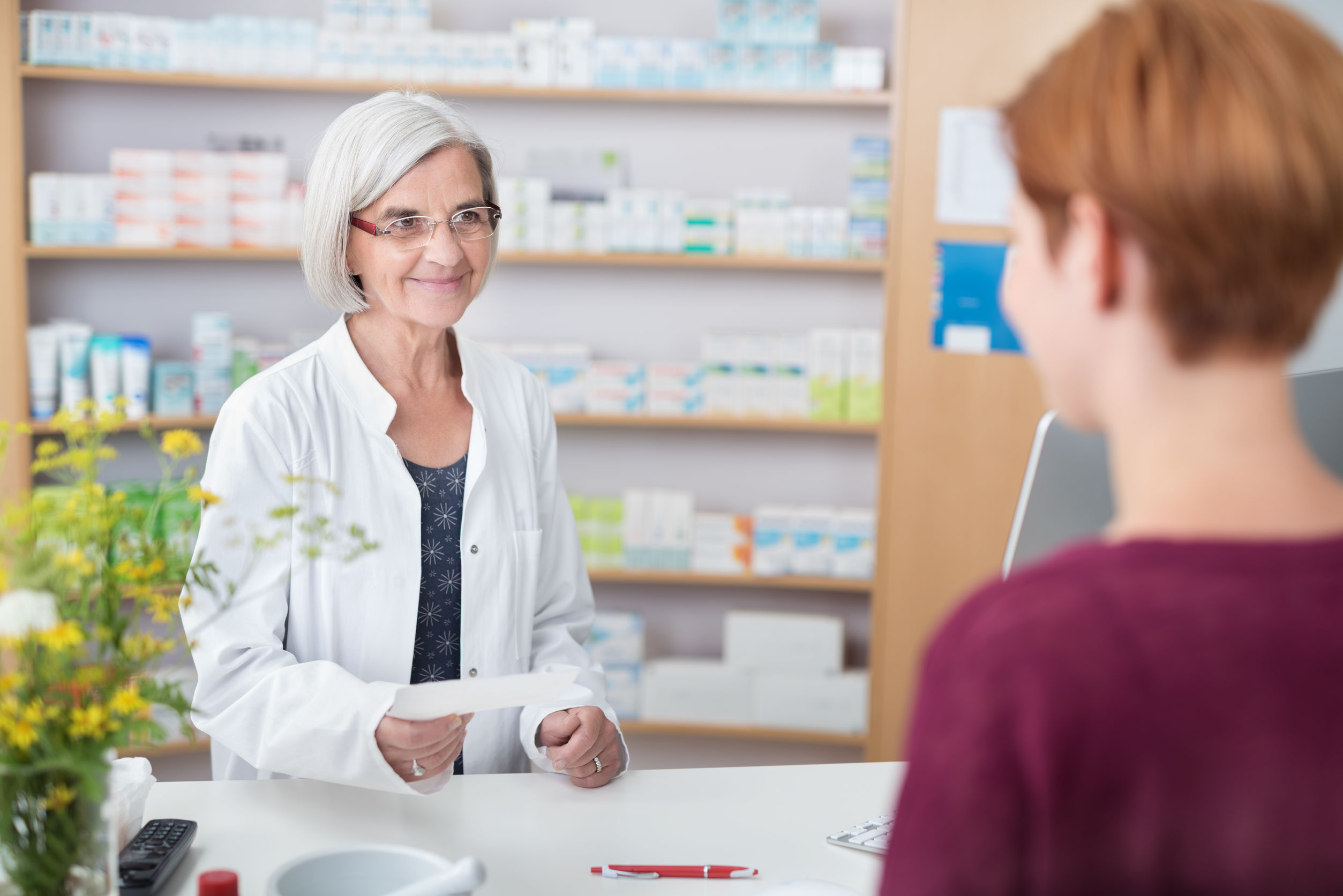 Friendly female pharmacist standing behind her counter at the pharmacy helping a client with a doctors prescription