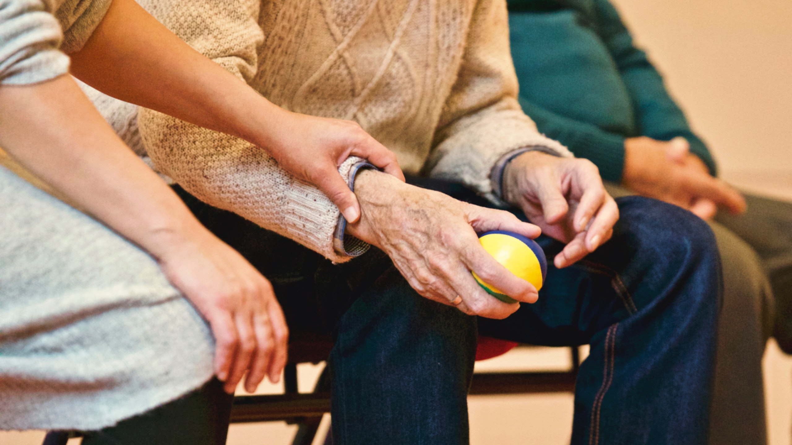 Old man squeezing stress ball with partner and caregiver