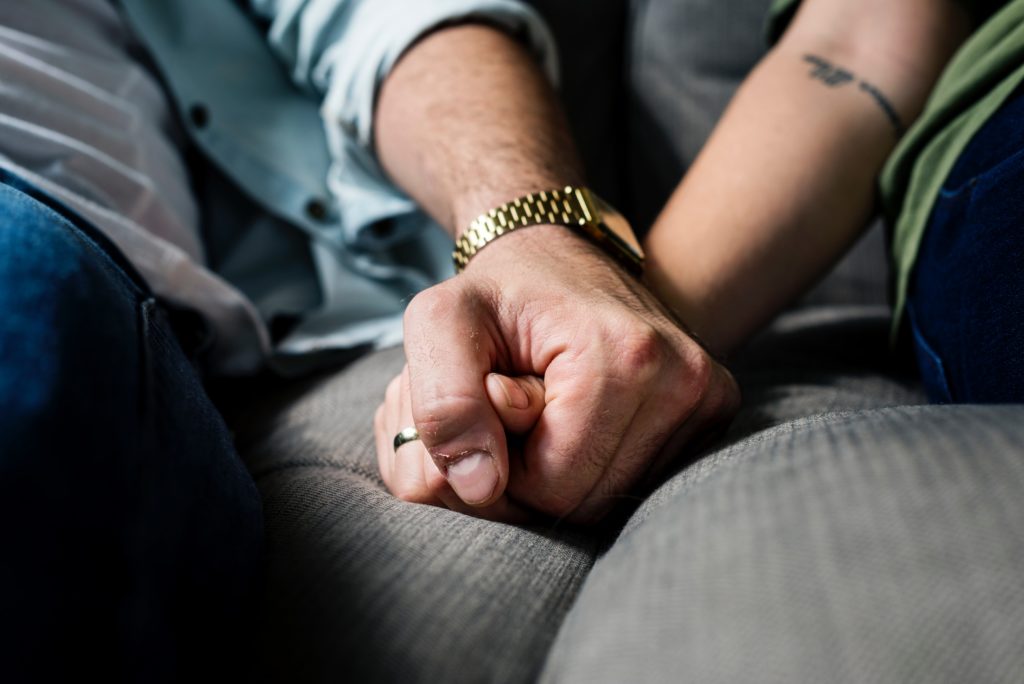 Two people holding hands against grey cushion