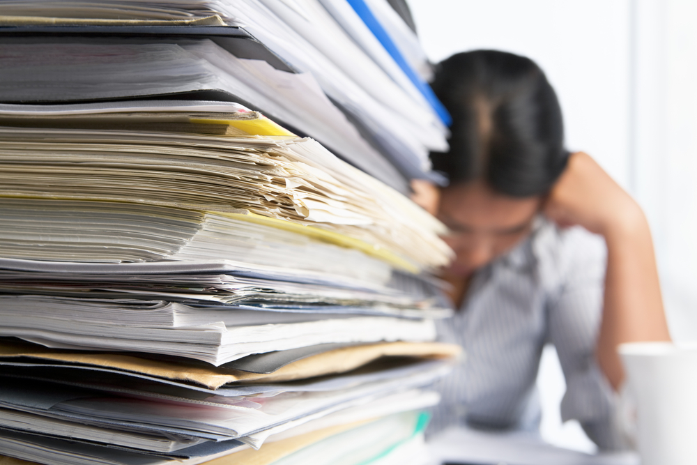 Foreground of stacks of documents with stressed out woman in the background